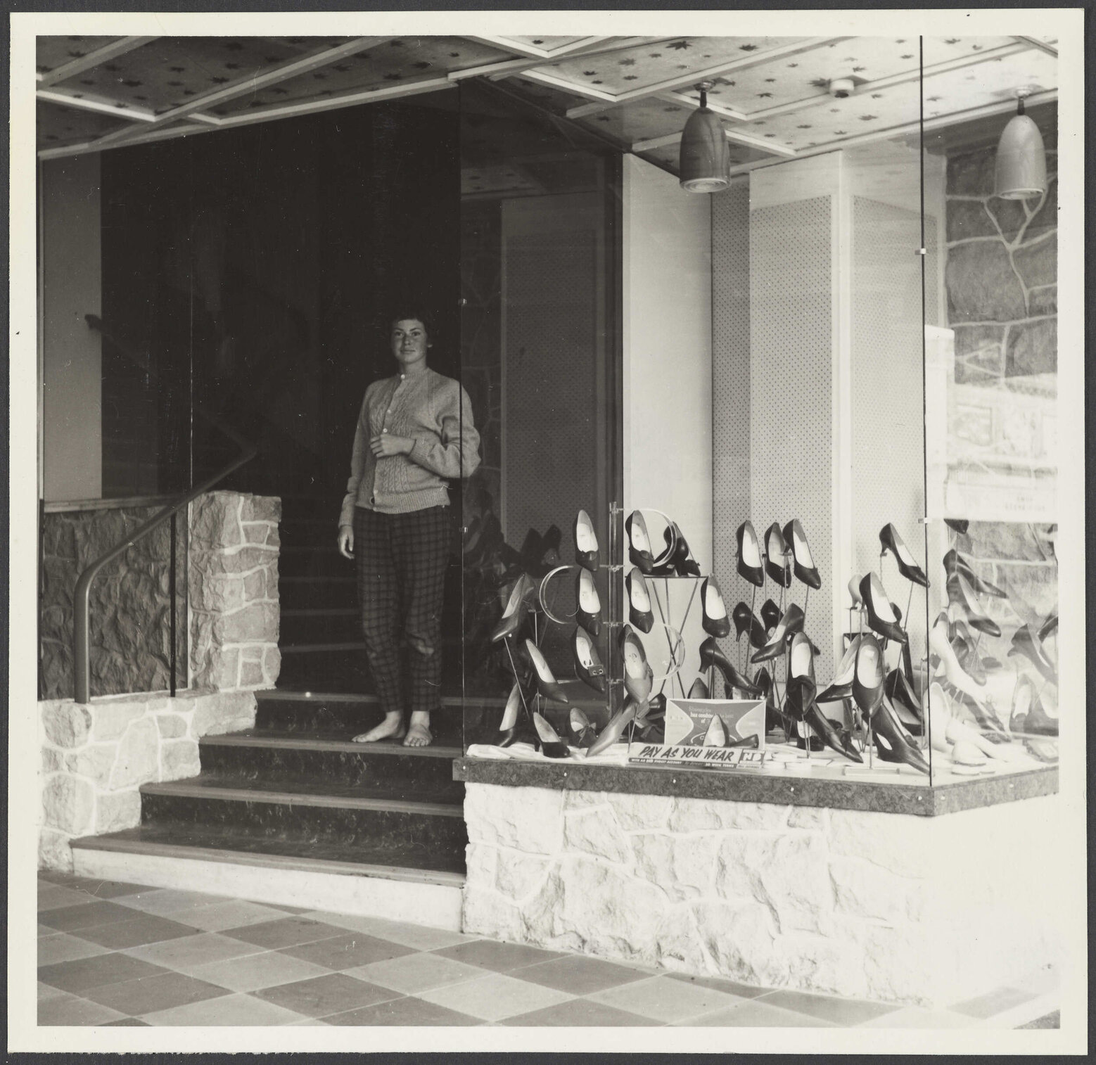 Window display of shoes and woman on staircase at Hallensteins, Hāwera