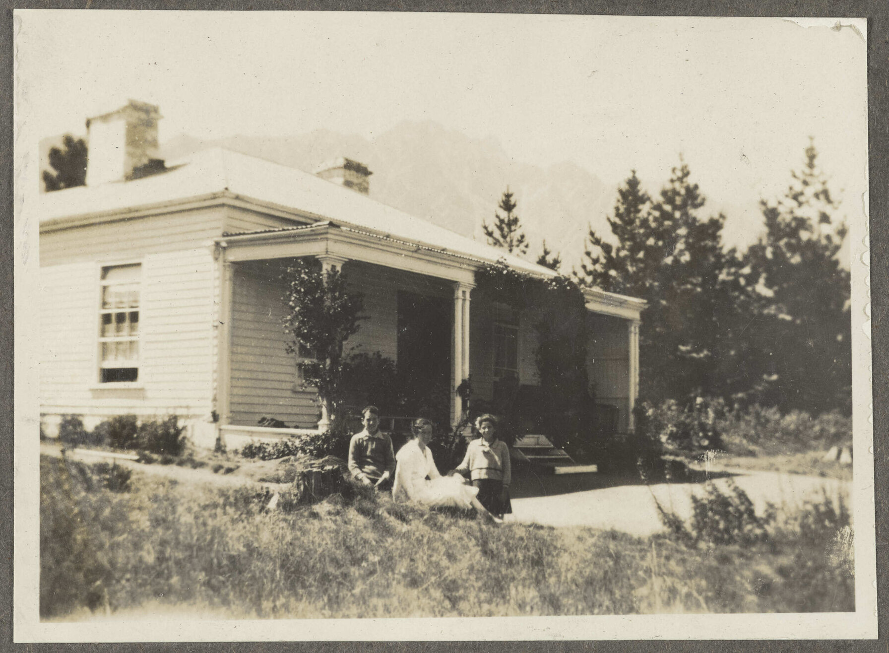 Three unidentified people sitting on porch in front of house