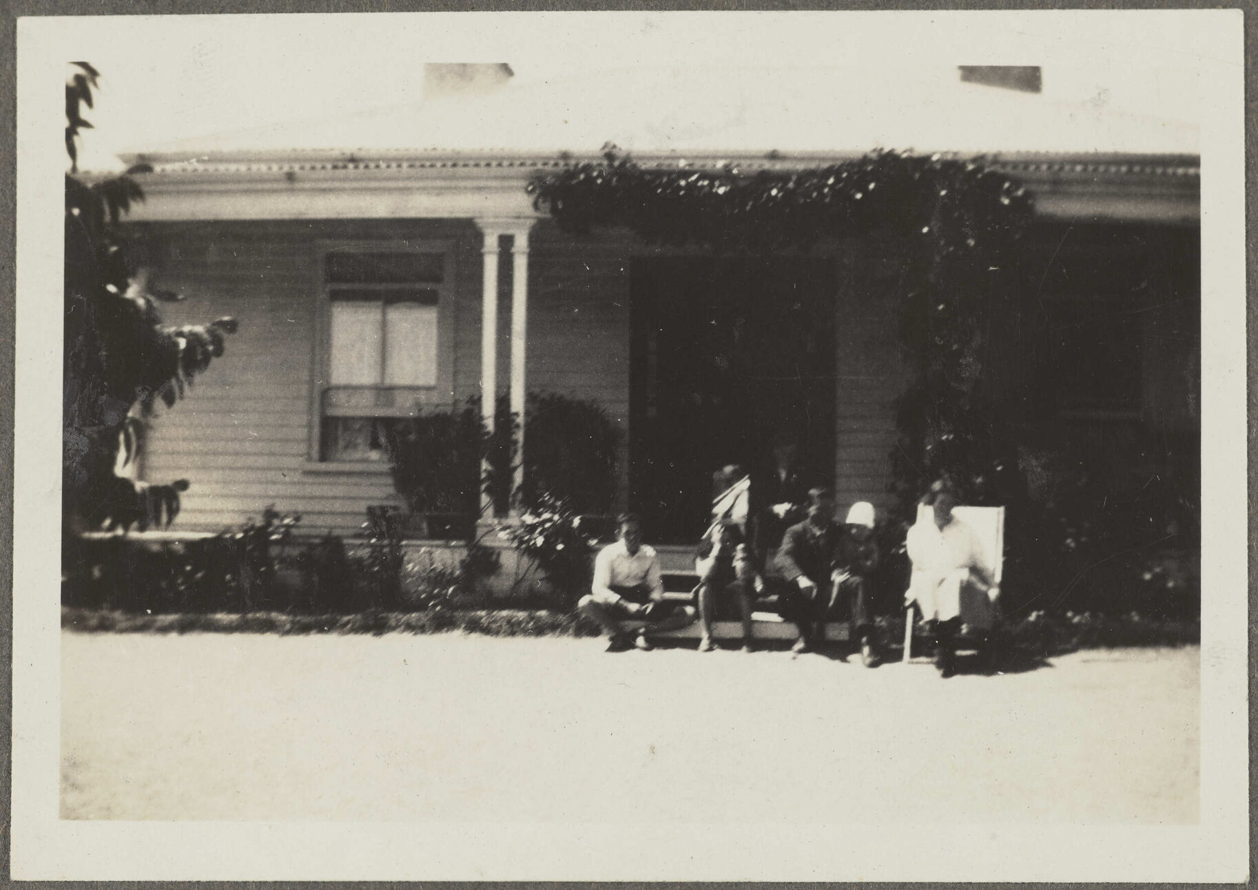 Five unidentified people sitting on porch of house