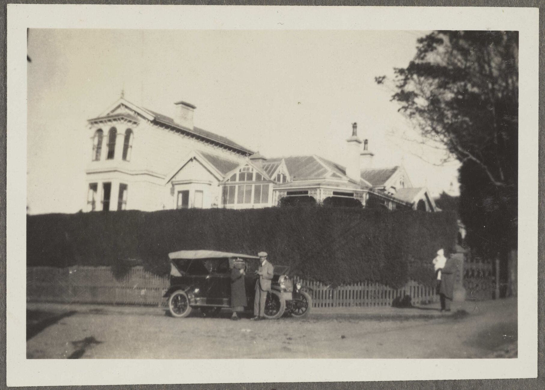 House with large hedge and car out front, with four unidentified people