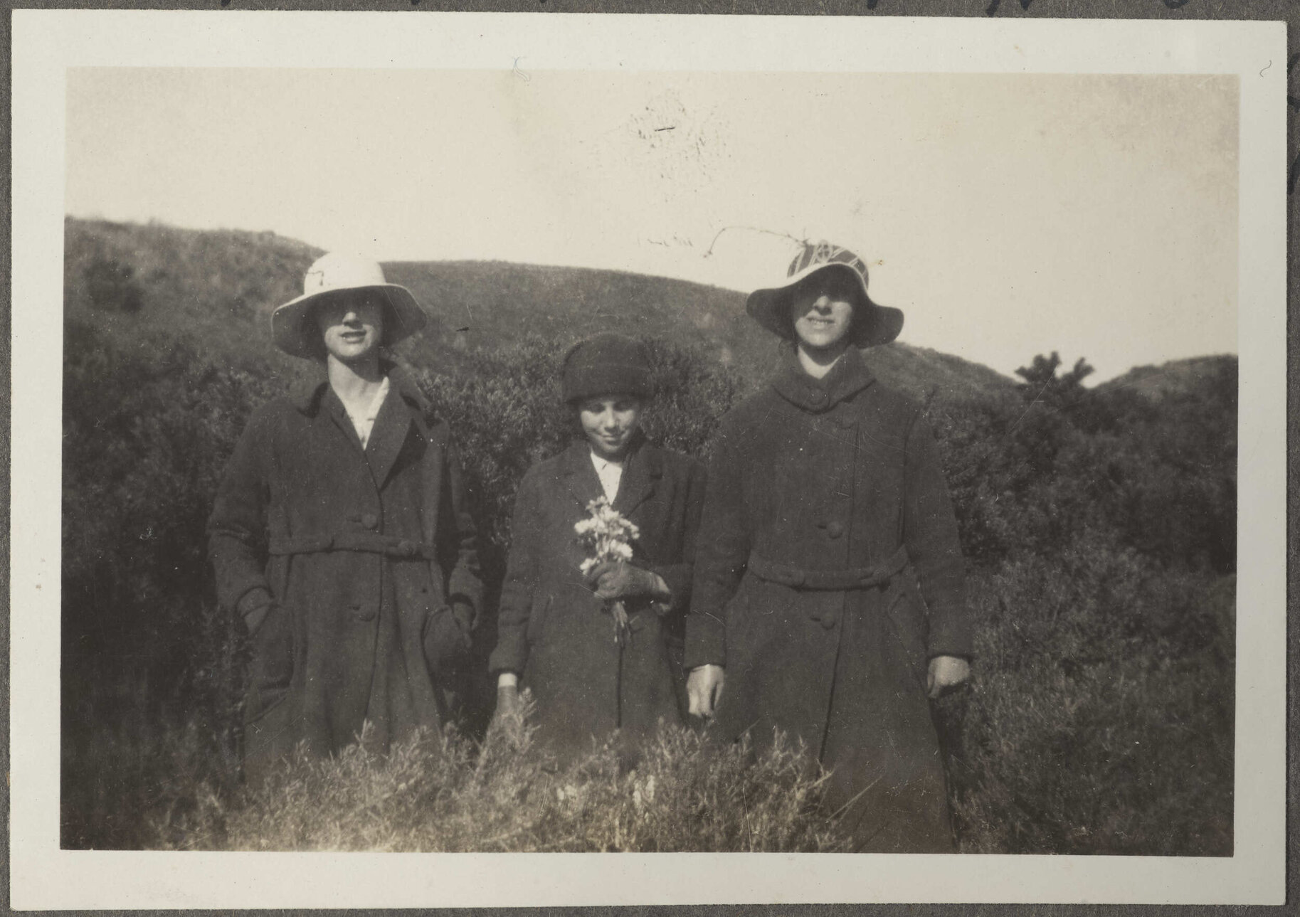 Three women in coats, one holding flowers
