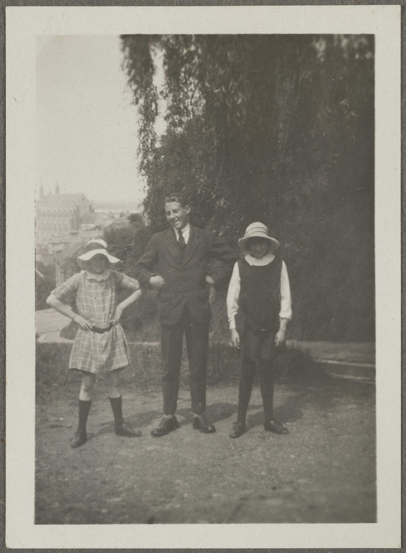 Charles Brasch and two unidentified girls, with large building in background
