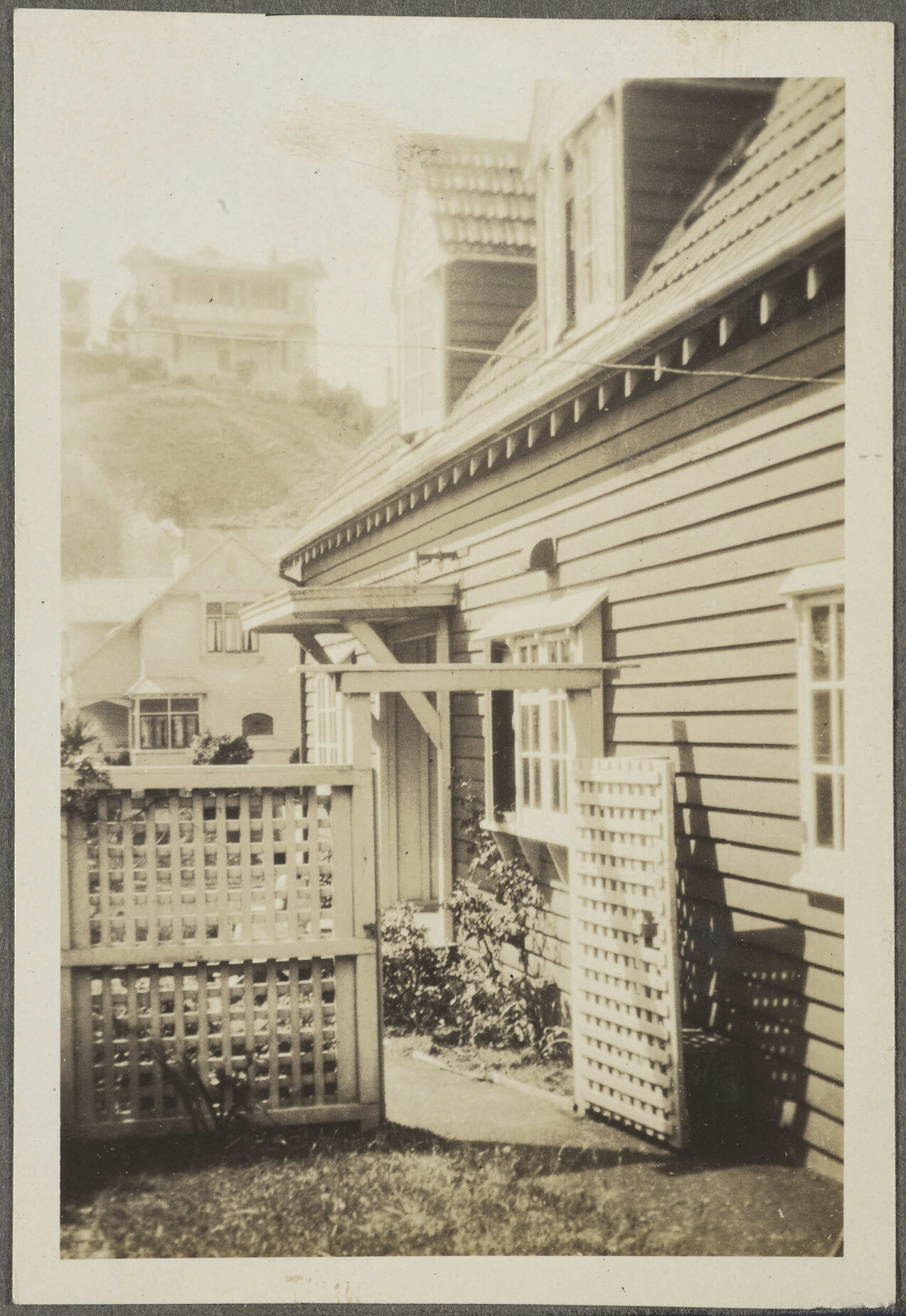 House with trellis and large house on hill in the background 
