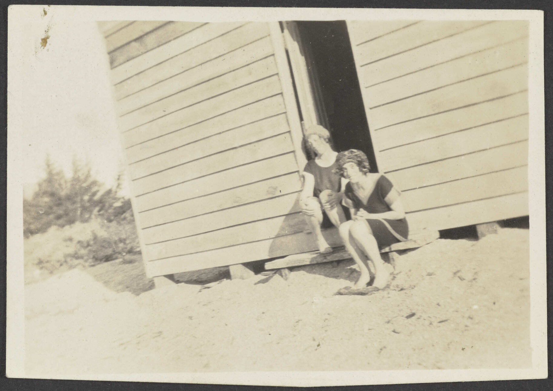 Two unidentified women sitting on step of wooden shack