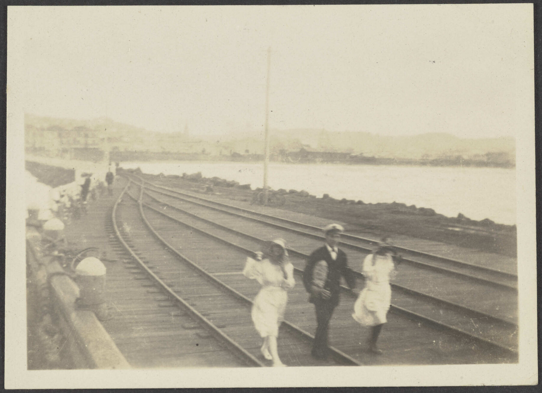 One man and two women walking along railway track by a harbour