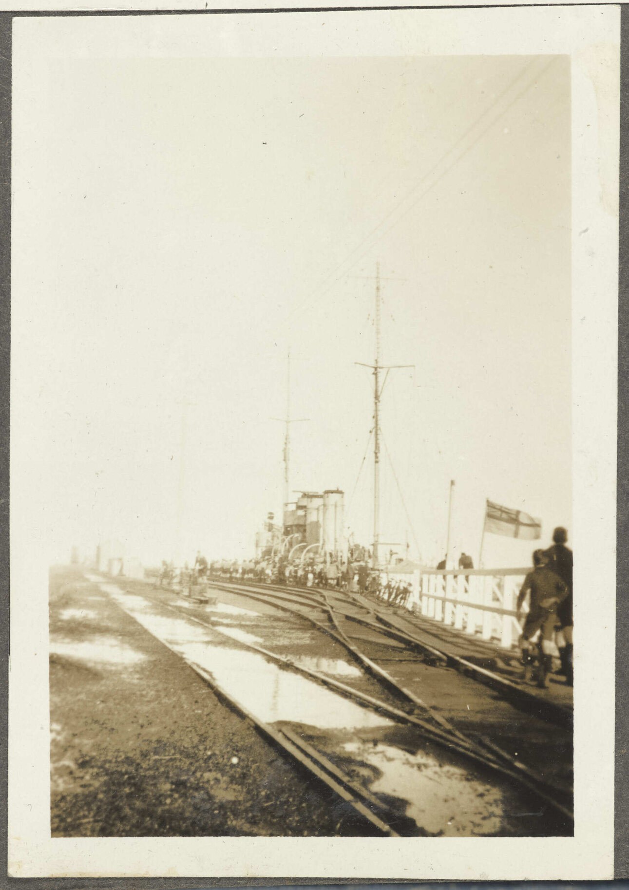 Railway tracks with boys by docked ship flying White Ensign