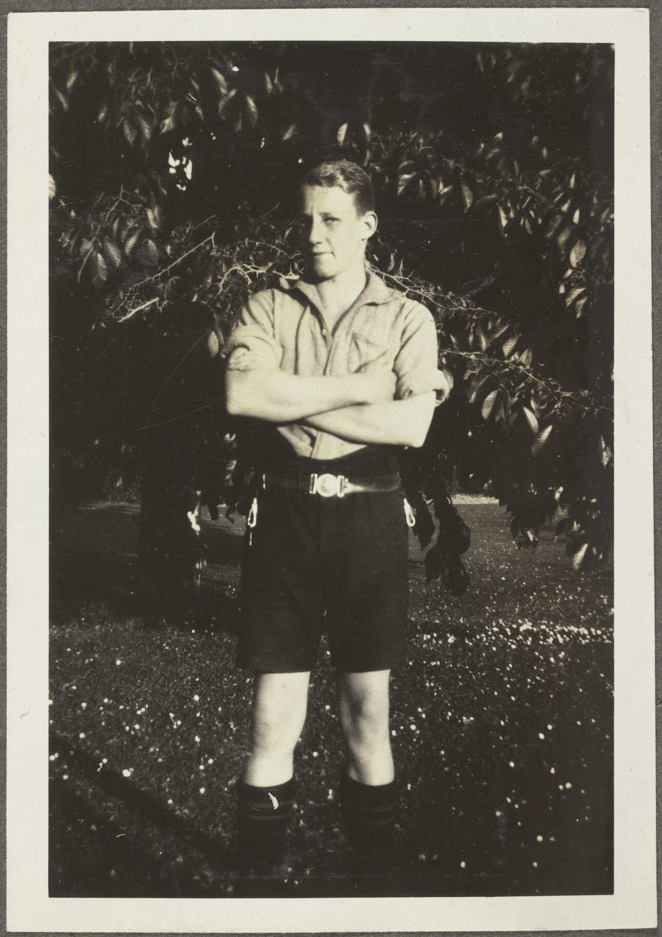 Boy standing cross-armed in front of a tree