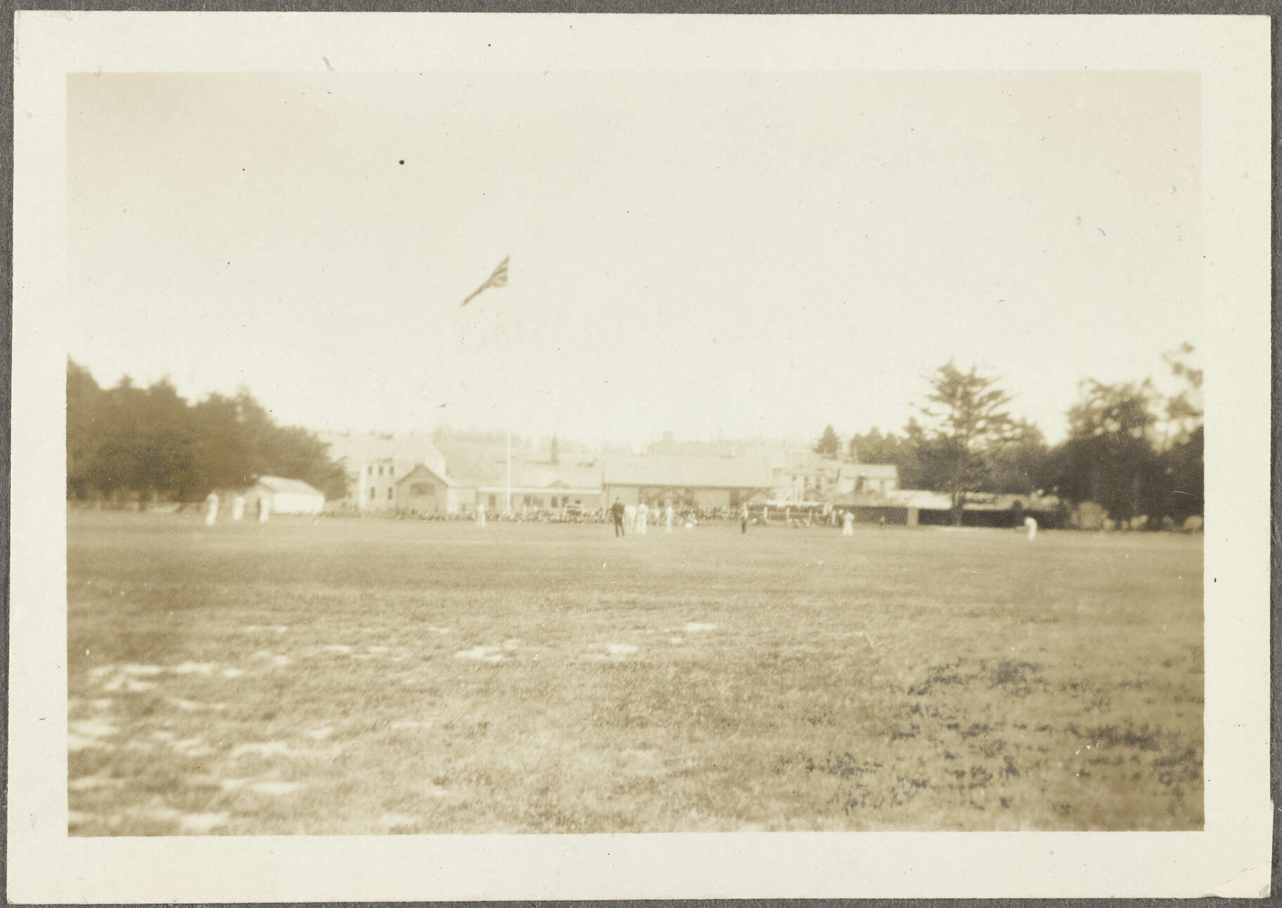 Cricket game looking towards [club rooms] flying Union Jack