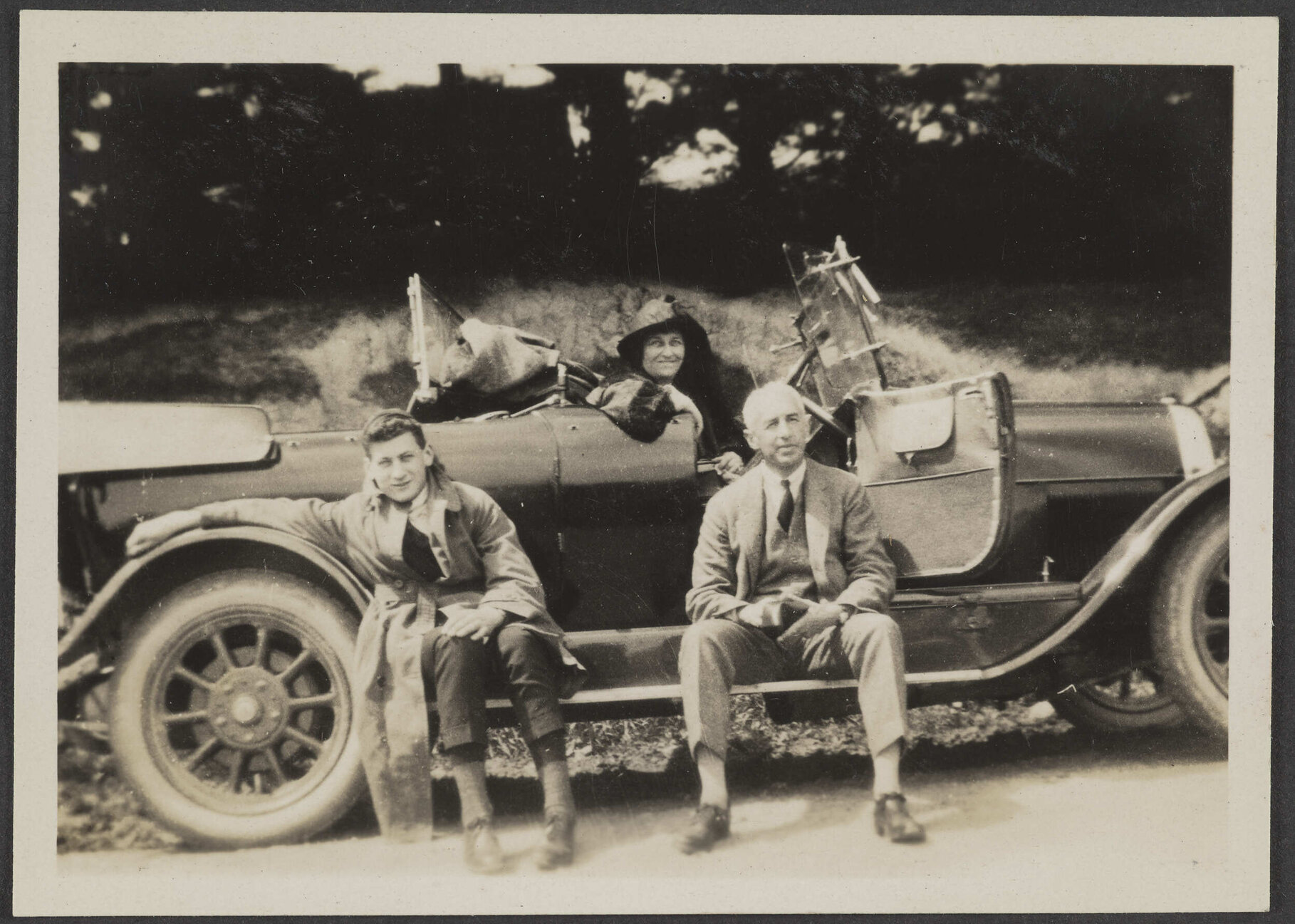 Henry Brasch sitting outside car, with two unidentified people
