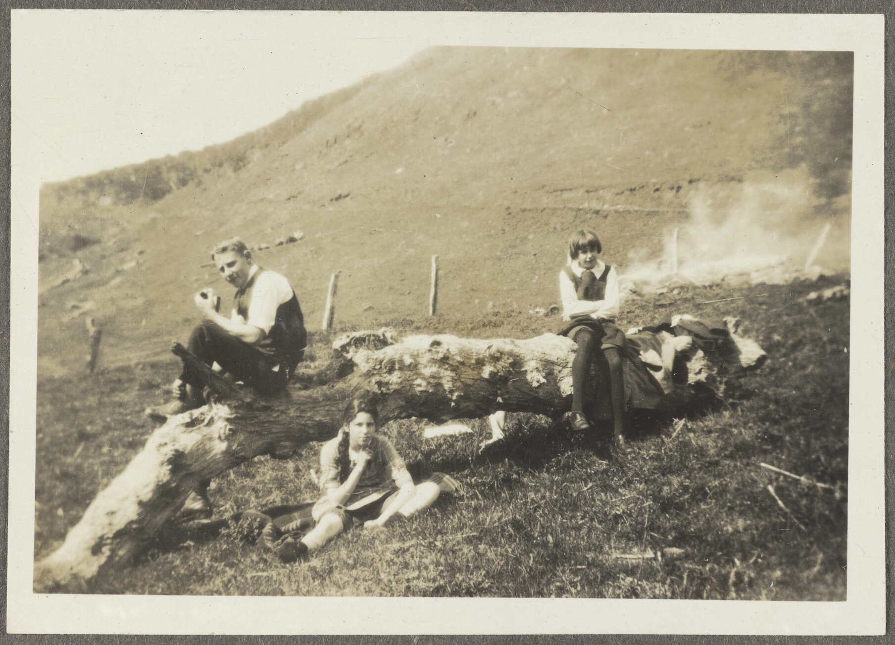 Lesley Brasch and two uidentified children sitting around large log