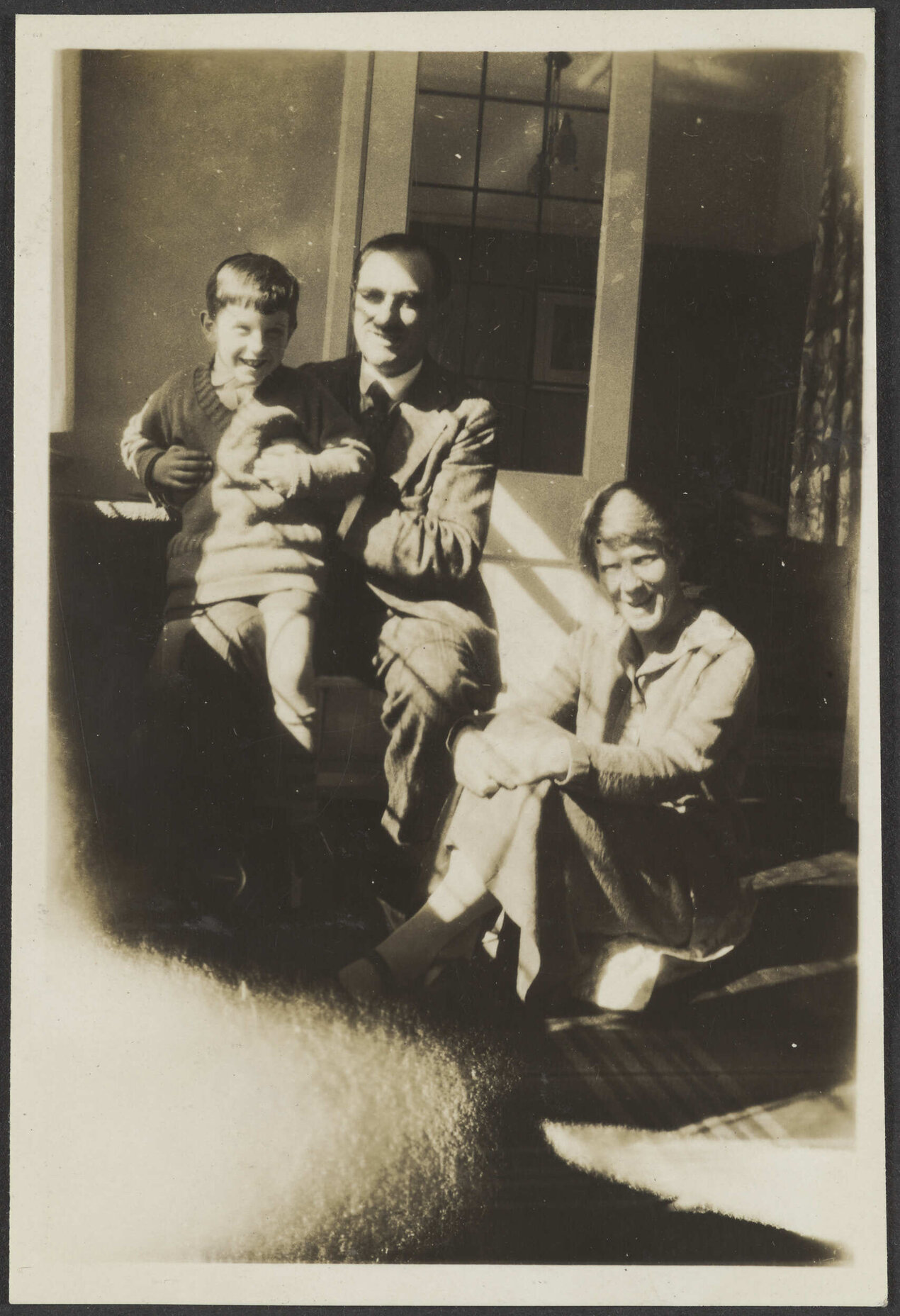 Unidentified man holding a small child, with unidentified woman on a porch