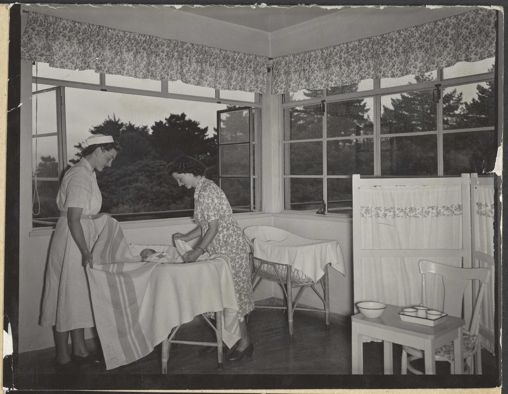 Nurse and mother [?] tucking baby into bassinet