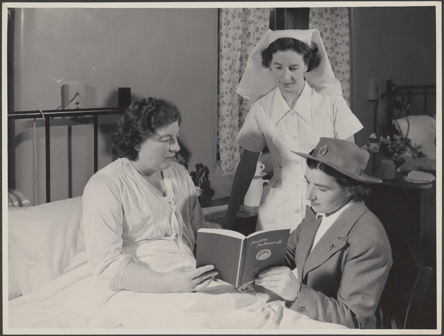 Two nurses and a mother reading "Modern Mothercraft"