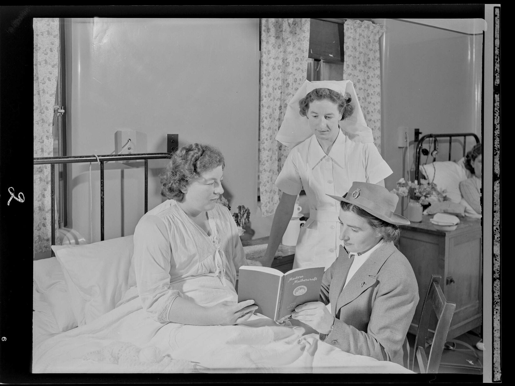 Two nurses and a mother reading "Modern Mothercraft"