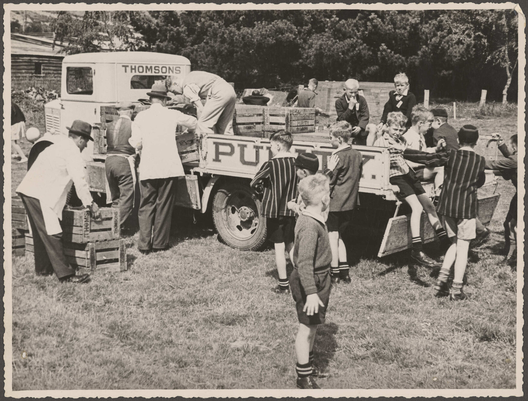Men unloading crates from the back of a Thomsons truck, surrounded by schoolboys