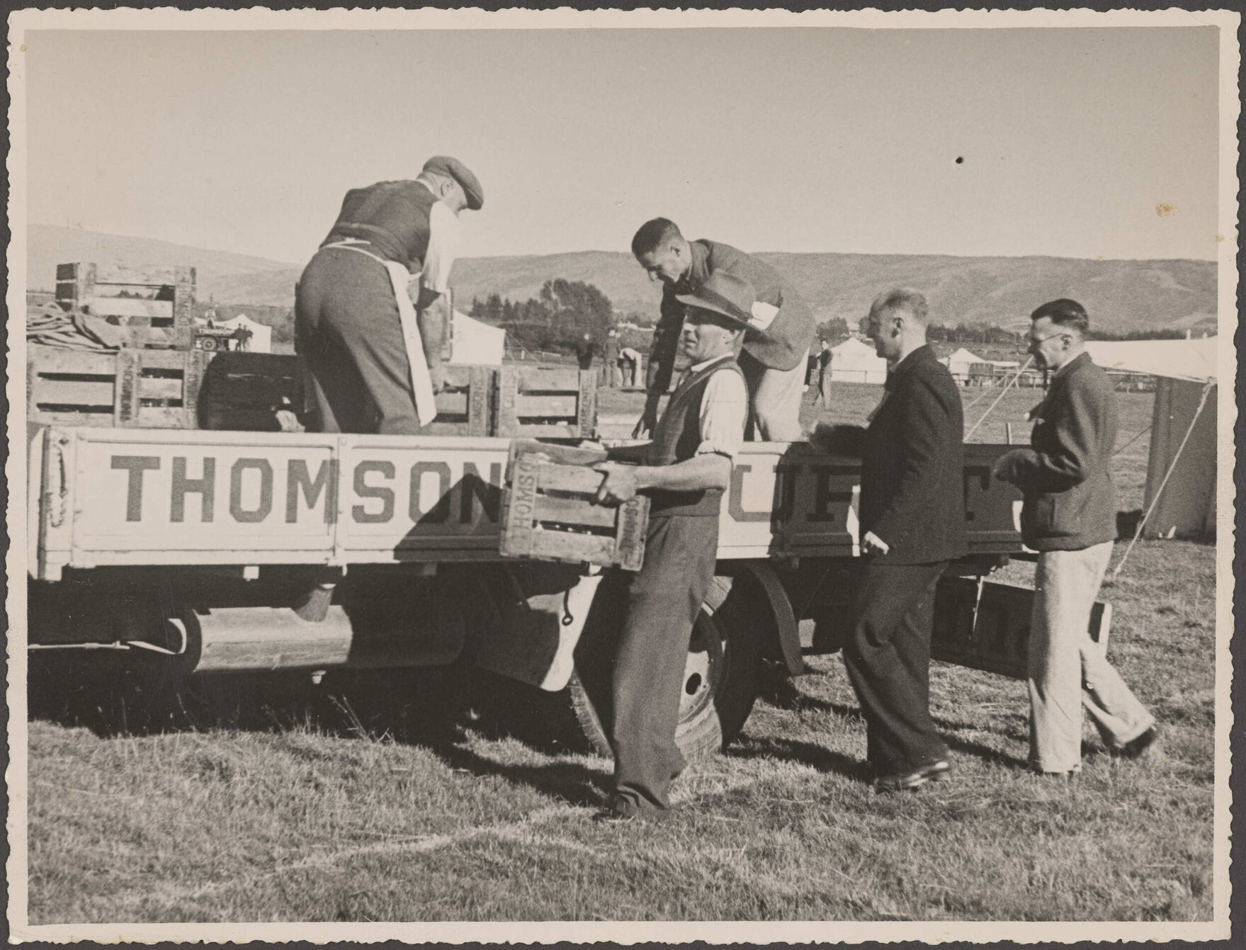Five men unloading crates from the back of a Thomsons truck