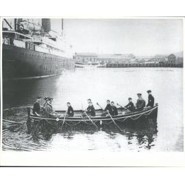Caption: 'The Sea Scouts' new boat, "Foam Queen" at the Dunedin Wharf. The boat carries of sea scouts in the Dominion. Seamanship instructor, H. R. Cole (in the stern) with District Commander Jones and Scoutmaster M'Pherson [? in the bow]