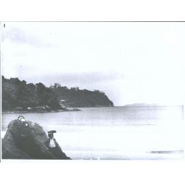 A woman gazes out from a rock on a beach
