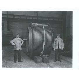 Men standing next to large spindle of cable