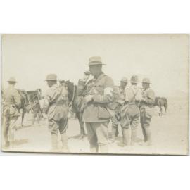 A group of soldiers, at least two with red cross arm bands, standing next to horses