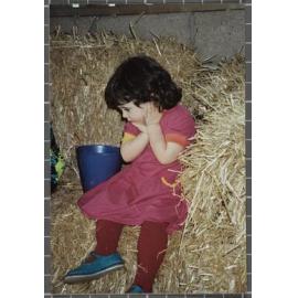 Young girl sitting on a hay bale, next to a bucket