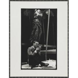 Man with glasses sitting cross-legged under angel figure, Downstage Theatre production of 'Heroes and butterflies'