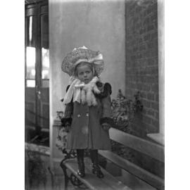 Em standing on garden seat wearing hat and coat