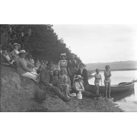 McGeorge family group of adults and children on the shore with a canoe, Karitane