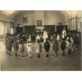 Children standing in circular formation, with two women in uniform