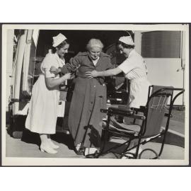 Two nurses helping an older woman out of an ambulance to a waiting chair
