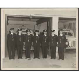 Seven men in St John uniform, with two ambulances behind