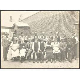 Group of male workers seated in front of brick building