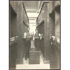 Two men in storage area with bobbins of yarn