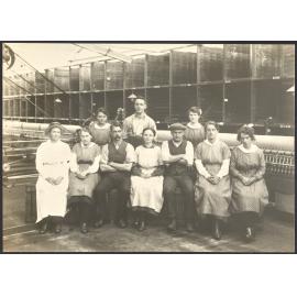 Staff group seated in front of spinning mule machinery