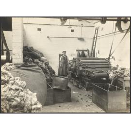 Worker with carding machine and piles of uncarded wool