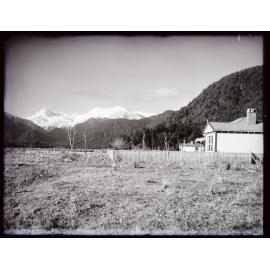 House and paddocks near a bush edge with snowy peaks behind
