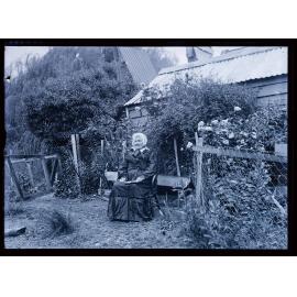 Older woman seated on a chair in the garden of a farmhouse