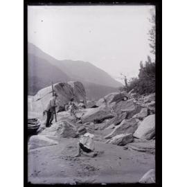 Three people on a sandy riverbank with boulders, Westland