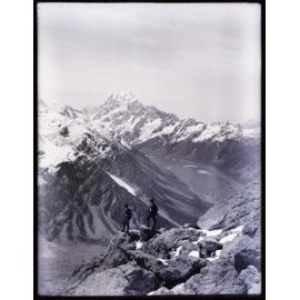 Two mountaineers standing on a rock outcrop, Sealy Range, with Aoraki / Mount Cook behind