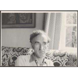Charles Brasch sitting on a couch