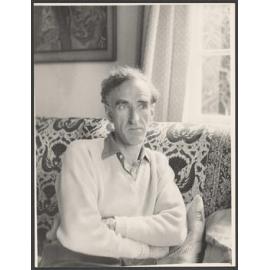 Charles Brasch sitting on a couch