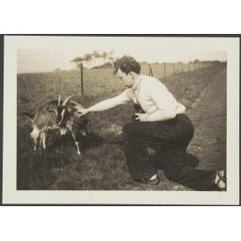 Man with camera and goat, in a rural setting