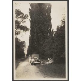 Group of people sitting by car parked on gravel road