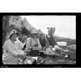 Five women and girls sitting on the ground outdoors