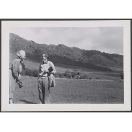 Charles Brasch and a woman in a paddock with hills in the background