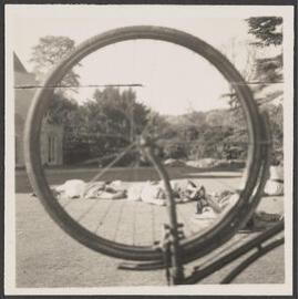Photograph taken through bicycle wheel of people lying on a lawn