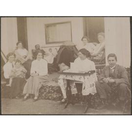 Family group sitting on a deck, with table and tea tray in foreground