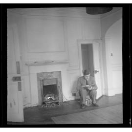 Man sitting by a fireplace reading [Roger Cox]