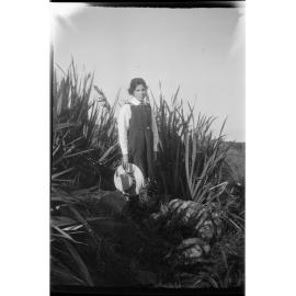 Lesley Brasch [?] standing in front of harakeke and holding a hat