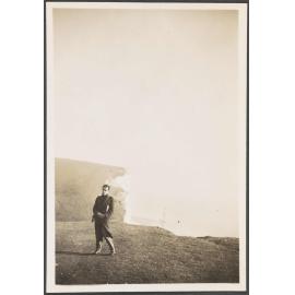 Charles Brasch standing in front of cliffs with a lighthouse in the distance